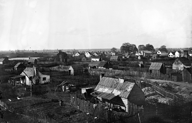 Wooden fencing weaves around a collection of small houses on a flat landscape.