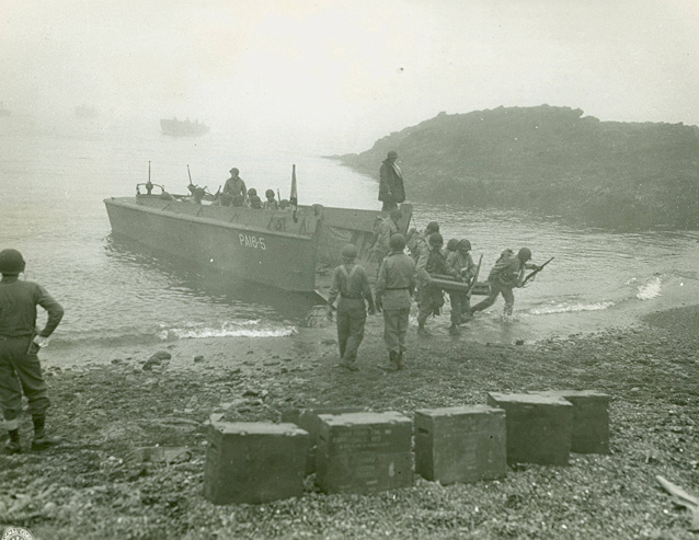 Uniformed soldiers carry gear off a boat onto a rocky beach. Uniformed soldiers carry gear off a boat onto a rocky beach.