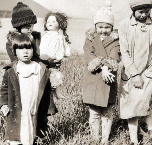 Four children captured on camera, one is carrying a doll.