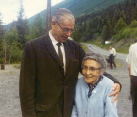 A man stands with his arm around an elderly woman.