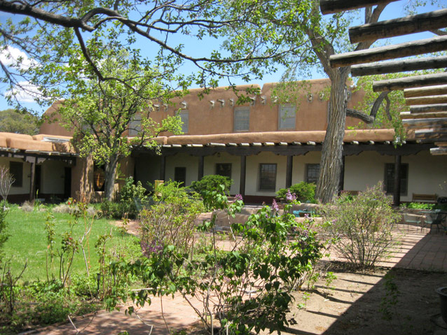 A courtyard with plants, trees, and lawn is surrounded by an adobe and stucco building.