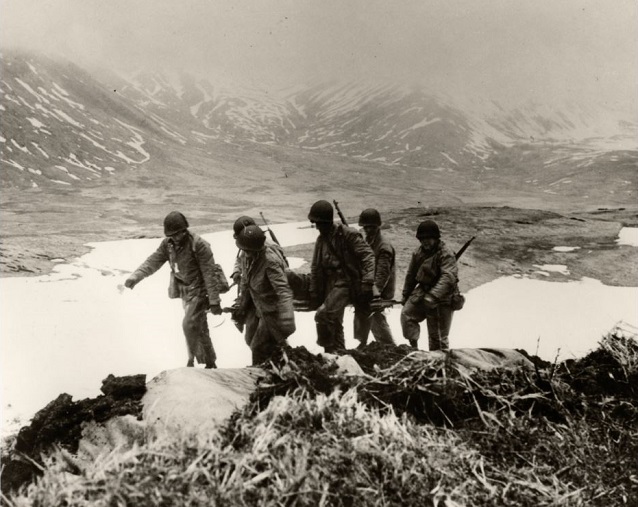 Six soldiers carry a stretcher with a wounded person.