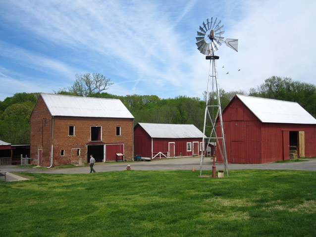 Wispy clouds above a windmill, farm buildings, and a bright green lawn. Wispy clouds above a windmill, farm buildings, and a bright green lawn.