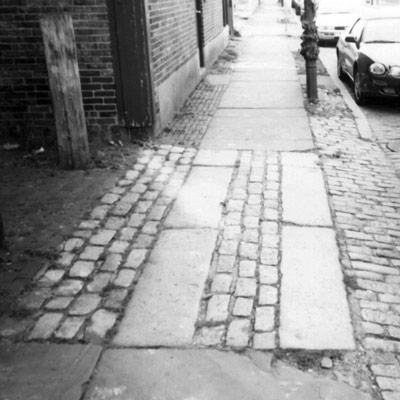 Parallel stones interrupt a cobblestone section of sidewalk.  