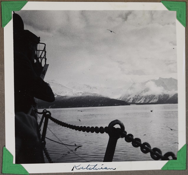 Black and white image of mountains across the water from behind a chain.