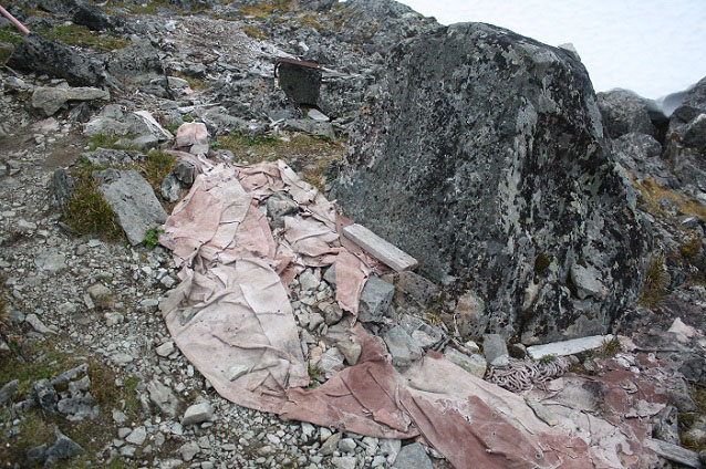 Canvas, rope, and wood strewn about a rocky area. Canvas, rope, and wood strewn about a rocky area.