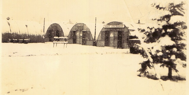 Quonset huts in the snow.  One building has sign 