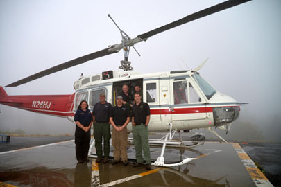 Men and women stand inside and outside of a helicopter on the ground.