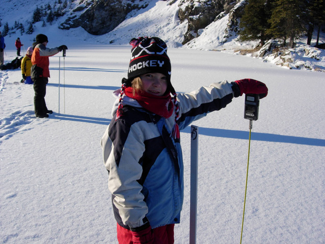 Young scientist taking measurements of ice and snow on a frozen lake.