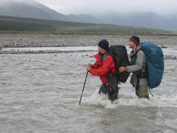 Two backpackers crossing a glacial river.