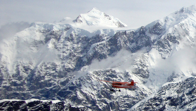 a small airplane flies amidst clouds near a mountain