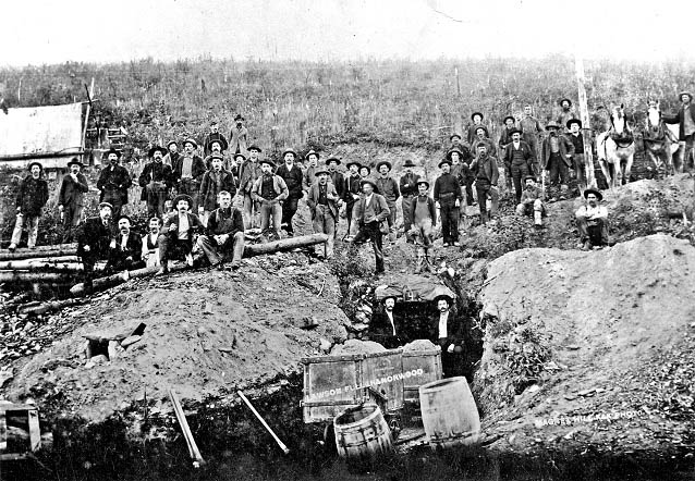 Black and white photo of men sitting in a mining area