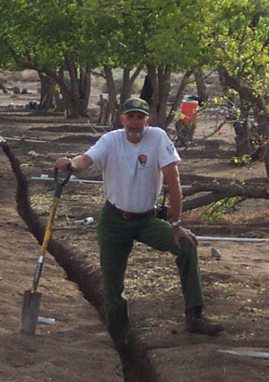 A man in NPS uniform poses with a shovel in an orchard.