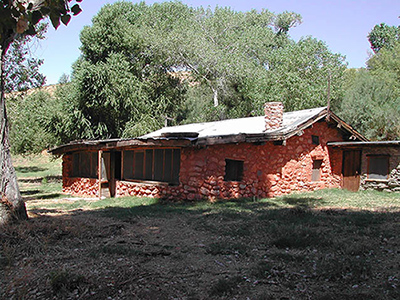 A single-story house of rough stone construction stands in the shade of leafy cottonwood trees. A single-story house of rough stone construction stands in the shade of leafy cottonwood trees.