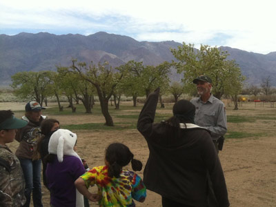 A group of young people gather in front of Gerry as he speaks to them in the orchard.