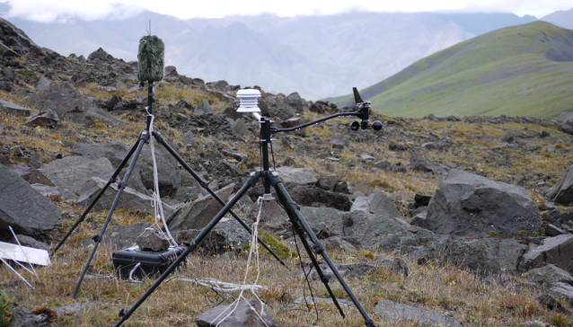 two tripods hold sound recording equipment sit on a rocky hillside