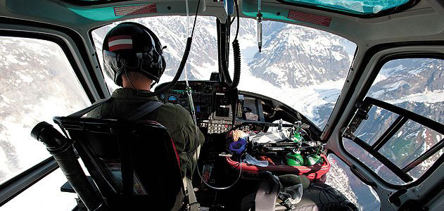 view of pilot from inside a helicopter flying over snowy mountains