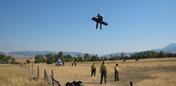 Ranger hanging from helicopter in the sky with materials for a rescue operation over a dry landscape