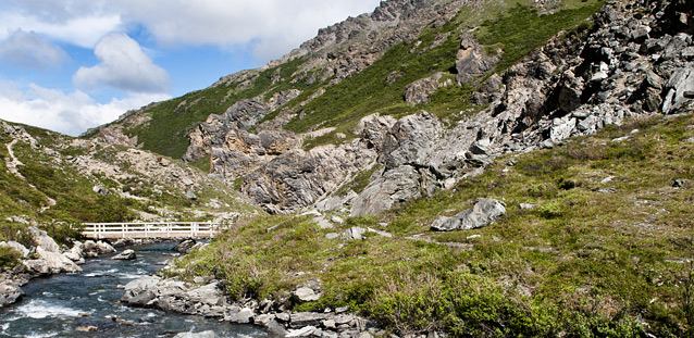 a river flows through a valley and under a trail bridge