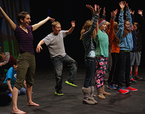 Children on a stage lift their arms above their heads.