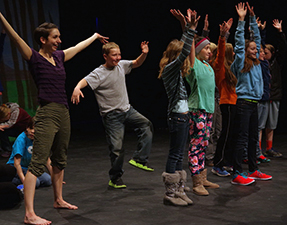 Children on a stage lift their arms above their heads. Children on a stage lift their arms above their heads.