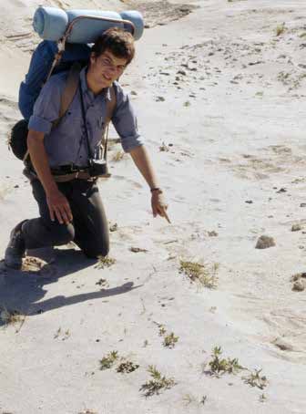 man wearing a backpack kneeling in sand