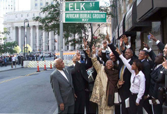 Group of African American people pointing at a street sign reading "African Burial Ground Way"