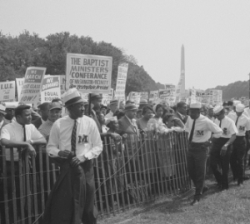 marchers with signs stand on far side of fence, B&W photo