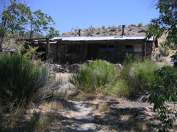 A single-story rustic cabin is constructed of stone and wood, surrounded by a dry landscape. A single-story rustic cabin is constructed of stone and wood, surrounded by a dry landscape.