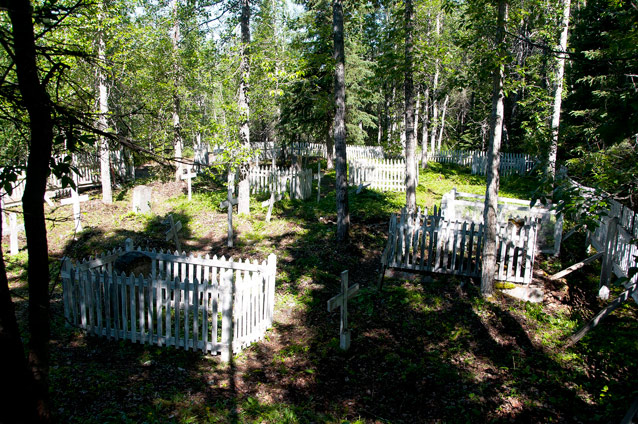 White fencing surrounds the perimeter and some of the headstones in a cemetery.