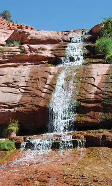 Water cascades down red rock faces at Navajo National Monument