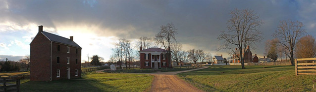 The setting sun lights up clouds over brick buildings of a rural landscape.