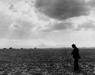 Black and white photo of a man walking through a field 