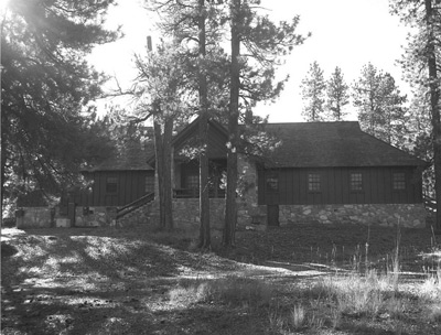 Pines surround a long lodge, made of wood with a rough stone foundation.