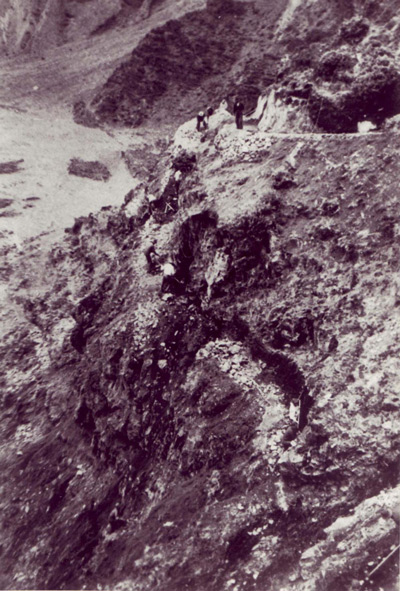 A high angle image shows tiny workers using shovels to create switchbacks on a rocky hillside.