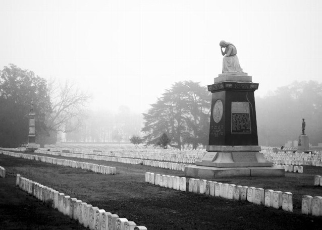 The marble Iowa Monument stands out above rows of white grave markers in a foggy cemetery.