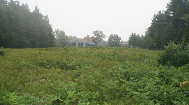 A low building is seen in the distance beyond an open expanse of low, green shrubs. (OCLP, 2008) A low building is seen in the distance beyond an open expanse of low, green shrubs. (OCLP, 2008)