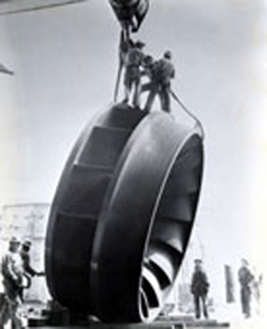 Black and white photo of workers standing on top of a waterwheel 