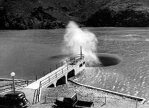 Black and white photo of boardwalk leading to a whirlpool with a fountain coming out 