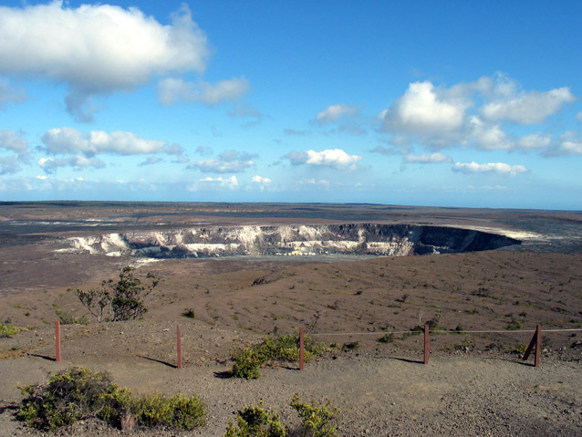 Soft blue sky and clouds hang over the Halemaumau Crater, a wide opening on the bare landscape. Soft blue sky and clouds hang over the Halemaumau Crater, a wide opening on the bare landscape.