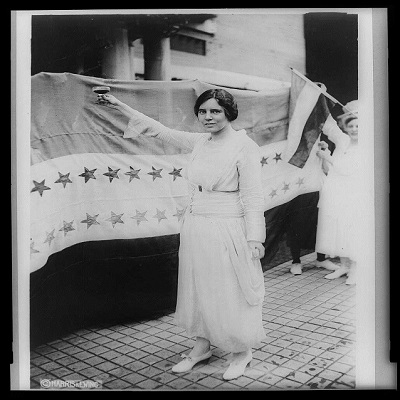 Black and white photo of a woman standing next to a flag