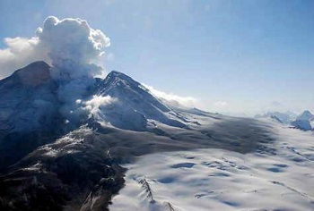 aerial side view of snow-covered volcano emitting gas