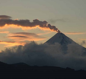 sideview of cone-shaped volcano emitting gas at sunset