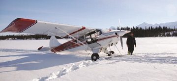 man stands next to a small plane in the snow