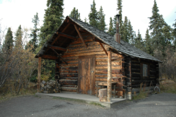 a log cabin in front of spruce trees a log cabin in front of spruce trees