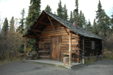 a log cabin in front of spruce trees