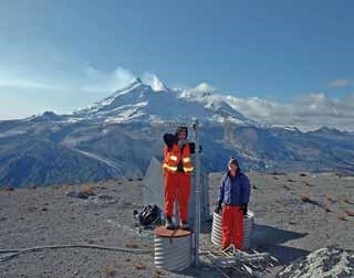 two women stand at the top of a seismic station with a snow-capped volcano in the distance two women stand at the top of a seismic station with a snow-capped volcano in the distance