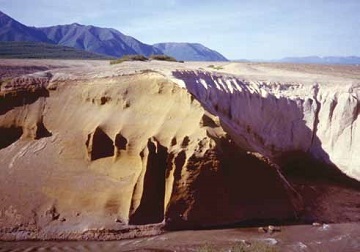 a yellow-brown sand hill next to a creek, with a paler deposit filling the former valley nearby