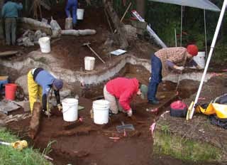 three people look at a layer of white ash in a cross-section of soil three people look at a layer of white ash in a cross-section of soil