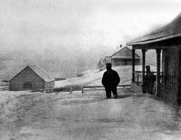 A man stands knee-deep in ash outside of a log porch A man stands knee-deep in ash outside of a log porch